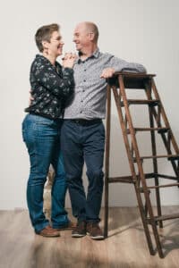 Photo par SL-Photographie d'un couple souriant, appuyé l'un contre l'autre à côté d'une échelle en bois, portant des jeans et des chemises imprimées dans un studio à Courtisols.