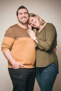Photographie en couleur par SL-Photographie d'un couple étreint, l'homme en pull bicolore et la femme en haut vert olive, rayonnant de bonheur dans un studio à Courtisols