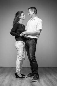 Portrait de SL-Photographie d'un couple échangeant un regard complice en noir et blanc, l'homme en chemise blanche et la femme en haut noir et pantalon clair, dans un studio à Courtisols.