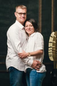 Image en couleur de SL-Photographie d'un couple en tenue décontractée blanche, se tenant dans une pièce sombre avec un décor élégant, affichant un sourire naturel à Courtisols.