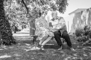 Photographie en noir et blanc par SL-Photographie d'un couple aîné assis sur un banc sous un arbre, dans une ambiance sereine en extérieur à Courtisols.