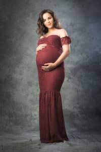 Femme rayonnante de maternité, en tenue de grossesse rouge bordeaux, éclairage doux qui souligne sa silhouette, par SL-Photographie à Châlons-en-Champagne.