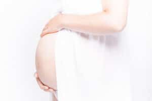 Femme enceinte vêtue de blanc rayonnant de sérénité, prise par SL-Photographie devant un fond immaculé, renforçant la pureté de la maternité
