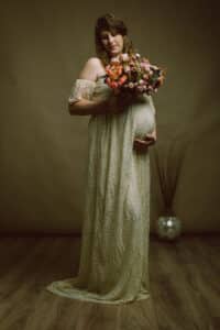 Future mère tenant un bouquet coloré, robe de dentelle crème, capturée par SL-Photographie dans un cadre intérieur apaisant à Châlons-en-Champagne.