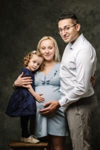 Shooting familial SL-Photographie : une future maman en robe bleue légère, accompagnée de son partenaire et de leur enfant, tous exprimant le bonheur