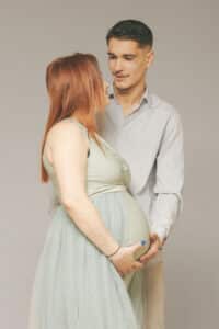 Couple attendri se tenant par la taille, la femme enceinte portant une robe longue vert pastel, capturé par SL-Photographie à Châlons-en-Champagne.
